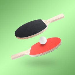 Image of Ping pong rackets and ball in air against light green background