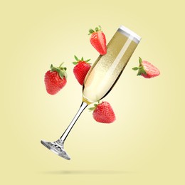 Image of Sparkling wine in flute glass and fresh strawberries falling against beige background