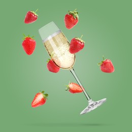 Image of Sparkling wine in glass and fresh strawberries falling against pastel green background