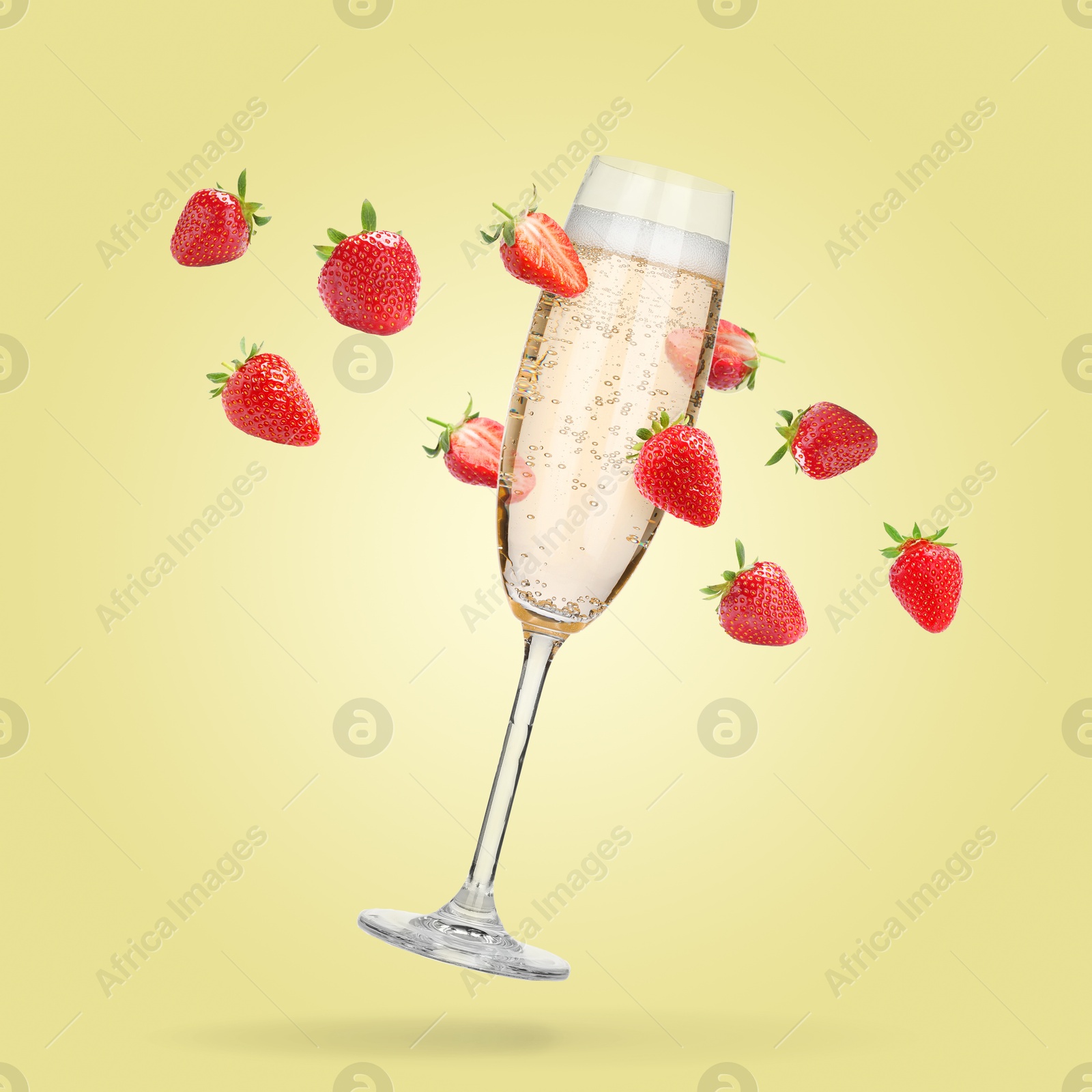 Image of Sparkling wine in flute glass and fresh strawberries falling against pastel yellow background