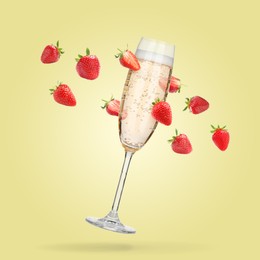 Image of Sparkling wine in flute glass and fresh strawberries falling against pastel yellow background