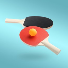 Image of Ping pong rackets and ball in air against light blue background