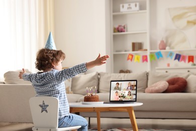 Image of Celebrating birthday online. Little boy with cake having video call with friends via laptop at home