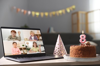 Image of Celebrating birthday online. Video call with children via laptop, cake and party hat on table indoors
