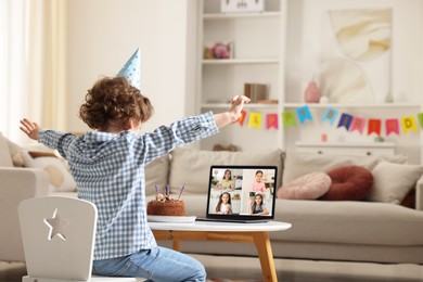 Image of Celebrating birthday online. Little boy with cake having video call with friends via laptop at home