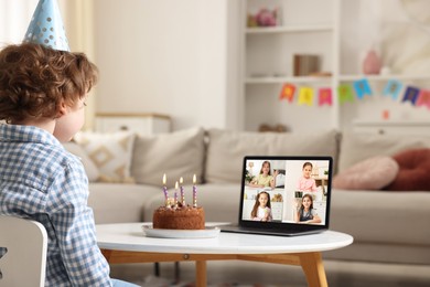 Image of Celebrating birthday online. Little boy with cake having video call with friends via laptop at home