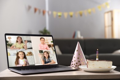 Image of Celebrating birthday online. Video call with children via laptop, cake and party hat on table indoors