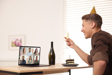 Image of Celebrating birthday online. Man with sparkling wine and cake having video call with friends via laptop at home