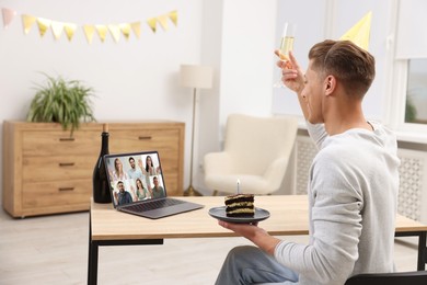 Image of Celebrating birthday online. Man with sparkling wine and cake having video call with friends via laptop at home
