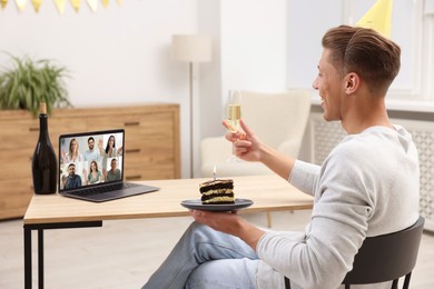 Image of Celebrating birthday online. Man with sparkling wine and cake having video call with friends via laptop at home
