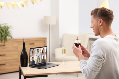 Image of Celebrating birthday online. Man with cupcake having video call with friends via laptop at home