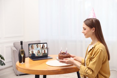 Image of Celebrating birthday online. Woman with cake having video call with friends via laptop at home