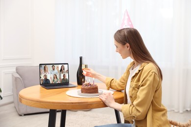 Image of Celebrating birthday online. Woman with sparkling wine and cake having video call with friends via laptop at home