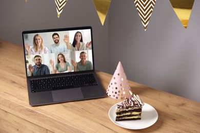 Image of Celebrating birthday online. Video call with friends via laptop, cake and party hat on table indoors