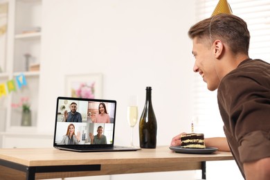 Image of Celebrating birthday online. Man with cake having video call with friends via laptop at home