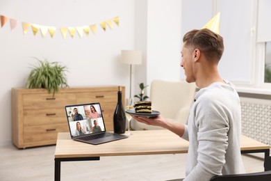 Image of Celebrating birthday online. Man with cake having video call with friends via laptop at home