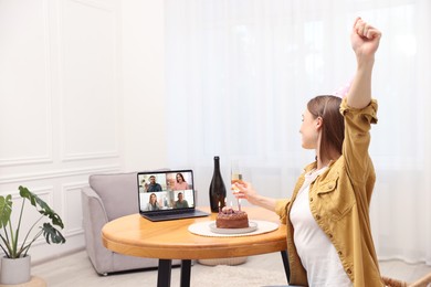Image of Celebrating birthday online. Woman with sparkling wine and cake having video call with friends via laptop at home