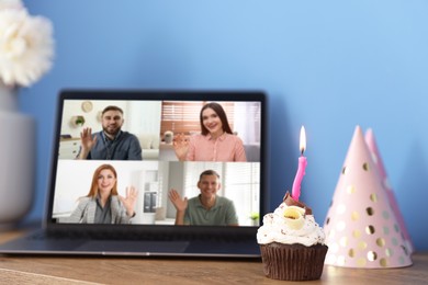 Image of Celebrating birthday online. Video call with friends via laptop, cupcake and party hat on table indoors
