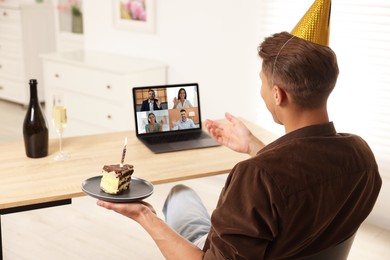 Image of Celebrating birthday online. Man with cake having video call with friends via laptop at home