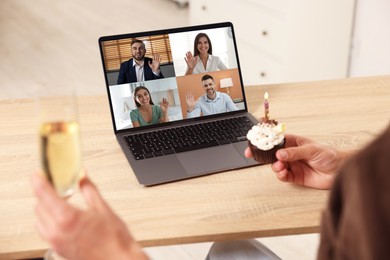 Image of Celebrating birthday online. Man with sparkling wine and cupcake having video call with friends via laptop at home, closeup