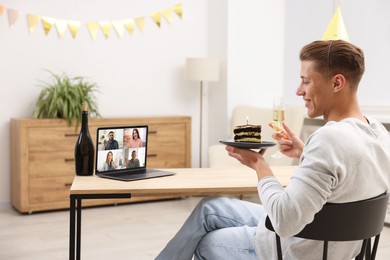 Image of Celebrating birthday online. Man with sparkling wine and cake having video call with friends via laptop at home