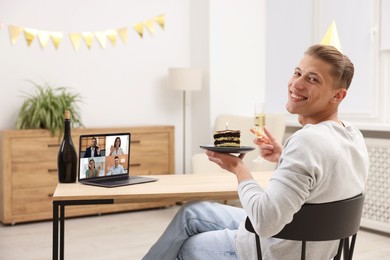 Image of Celebrating birthday online. Man with sparkling wine and cake having video call with friends via laptop at home