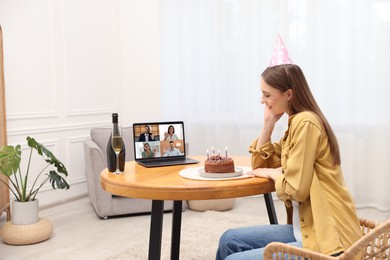 Image of Celebrating birthday online. Woman with sparkling wine and cake having video call with friends via laptop at home