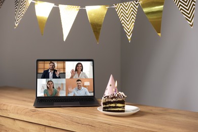 Image of Celebrating birthday online. Video call with friends via laptop, cake and party hat on table indoors