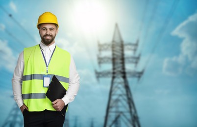 Image of Power engineer in hard hat holding clipboard against high voltage towers