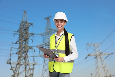 Image of Power engineer in hard hat holding clipboard against high voltage towers