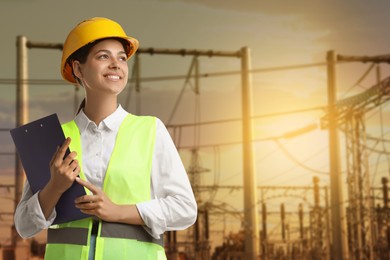 Image of Power engineer in hard hat holding clipboard against electrical substation