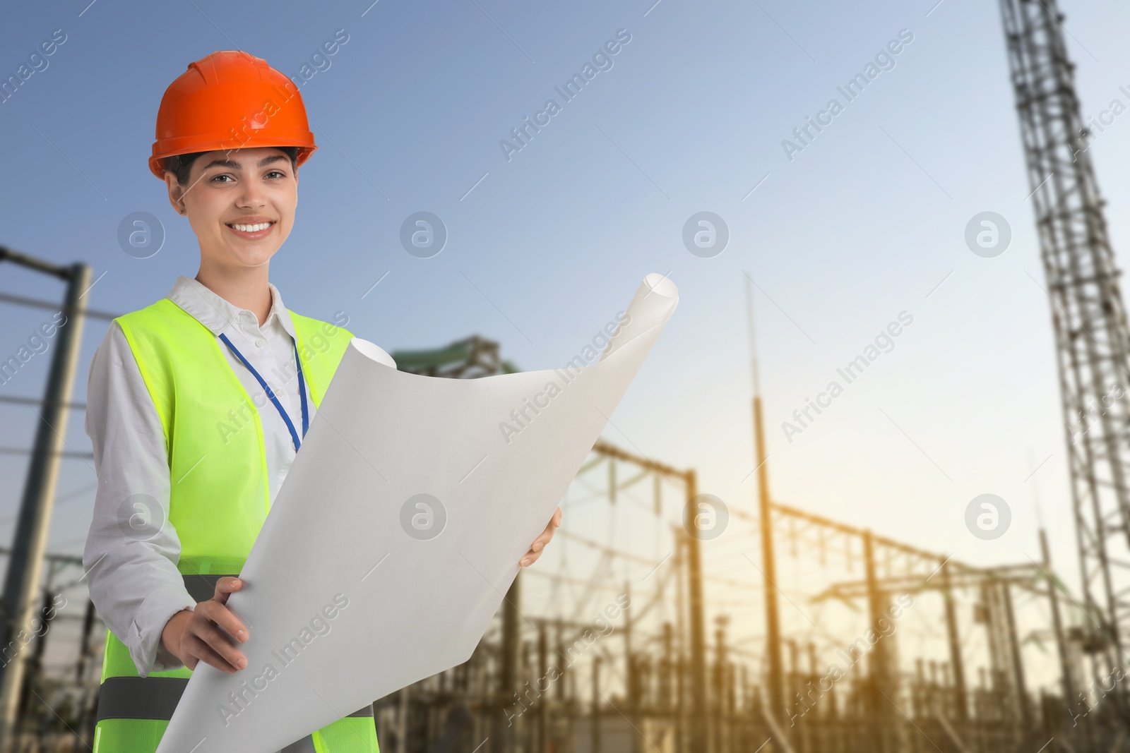 Power engineer in hard hat holding draft against electrical substation Image of Power engineer in hard hat holding draft against electrical substation