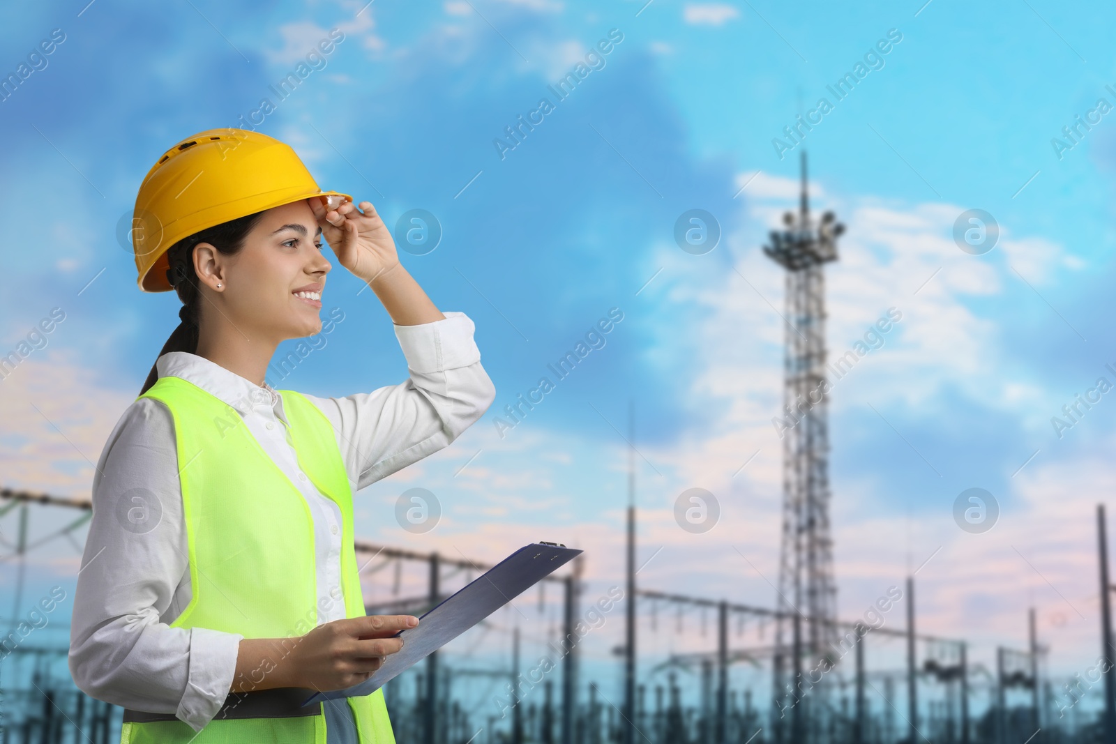 Power engineer in hard hat holding clipboard against electrical substation Image of Power engineer in hard hat holding clipboard against electrical substation