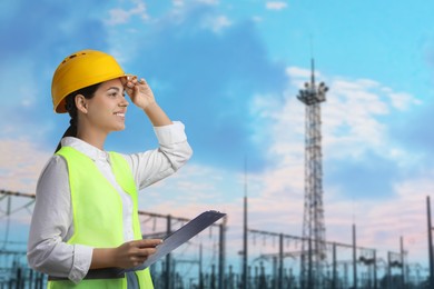 Image of Power engineer in hard hat holding clipboard against electrical substation