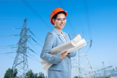 Image of Power engineer in hard hat holding drafts against high voltage towers