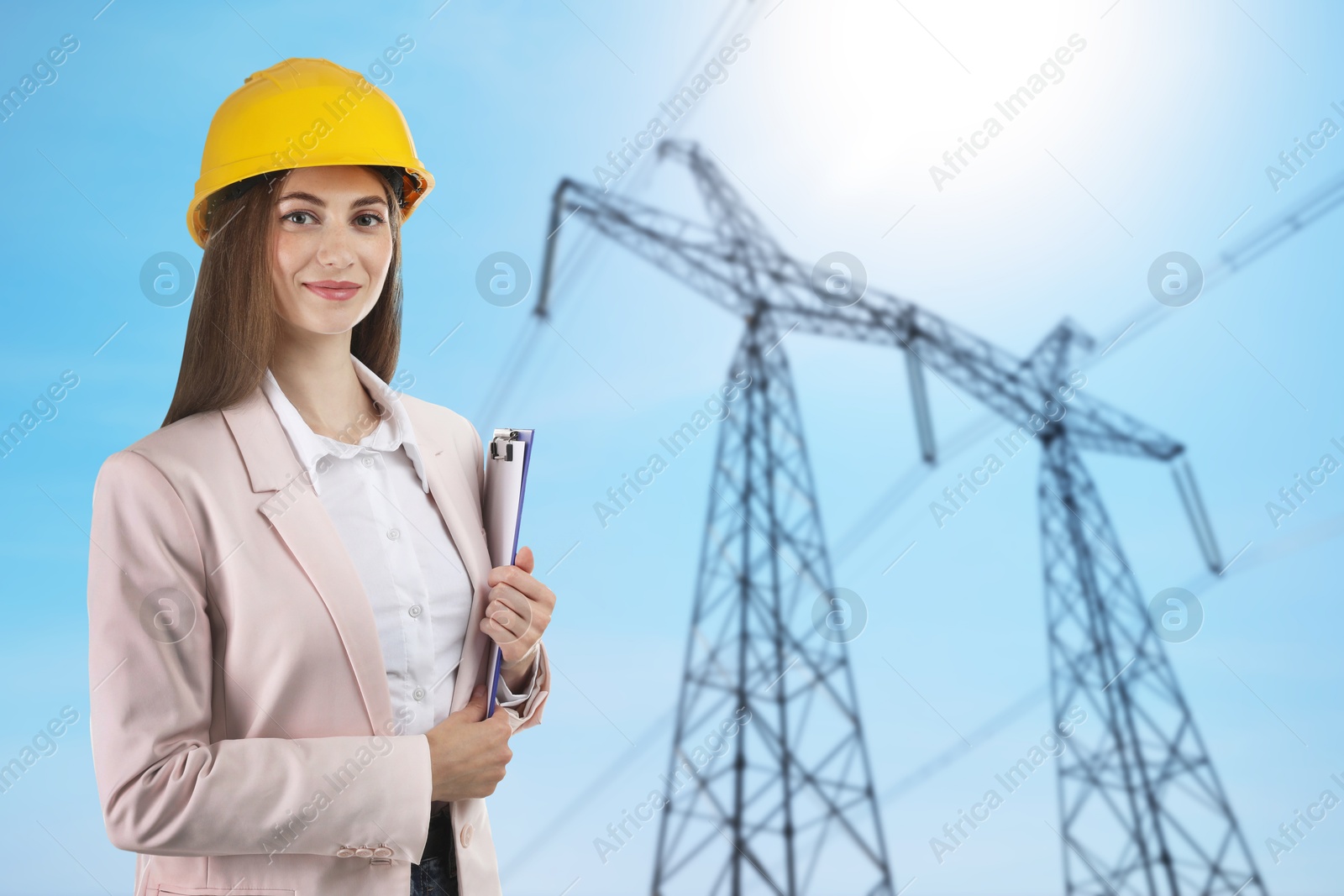 Power engineer in hard hat holding clipboard against high voltage tower Image of Power engineer in hard hat holding clipboard against high voltage tower