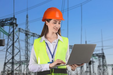 Image of Power engineer in hard hat holding laptop against electrical substation
