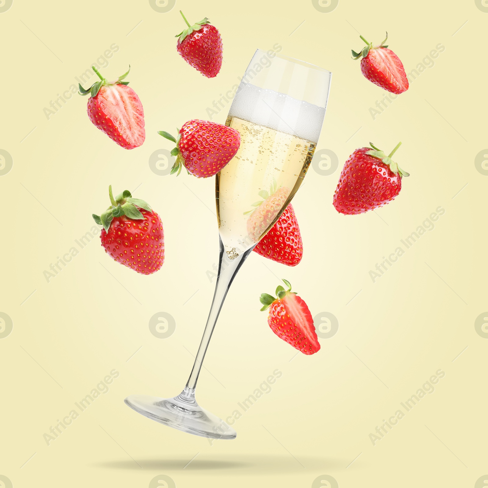 Sparkling wine in glass and fresh strawberries falling against beige background Image of Sparkling wine in glass and fresh strawberries falling against beige background