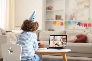 Image of Celebrating birthday online. Little boy with cake having video call with friends via laptop at home