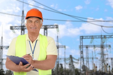 Image of Power engineer in hard hat holding clipboard against electrical substation