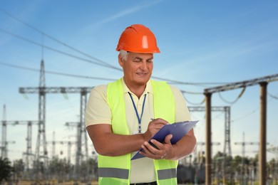 Image of Power engineer in hard hat holding clipboard against electrical substation