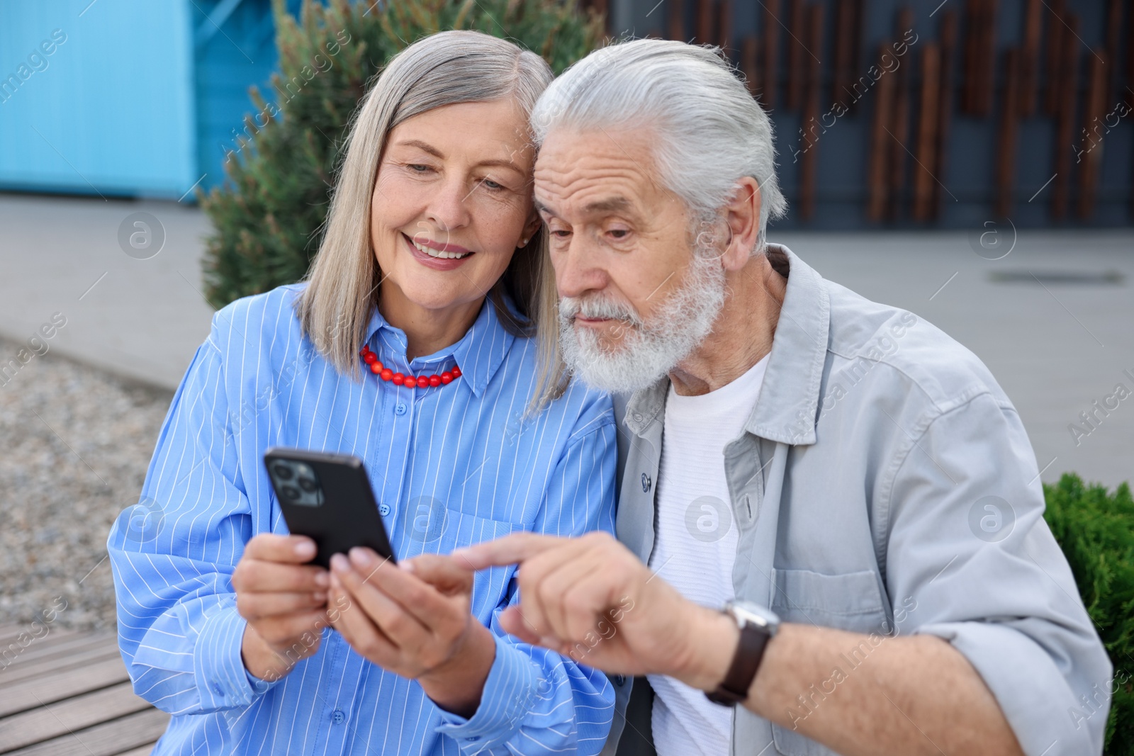 Lovely senior couple with smartphone on bench outdoors Photo of Lovely senior couple with smartphone on bench outdoors
