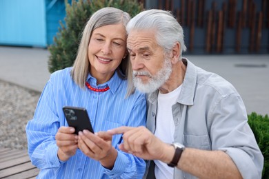 Photo of Lovely senior couple with smartphone on bench outdoors