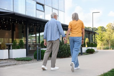 Photo of Lovely senior couple walking together near building outdoors, back view