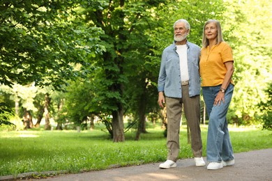 Photo of Lovely senior couple walking together in park, space for text