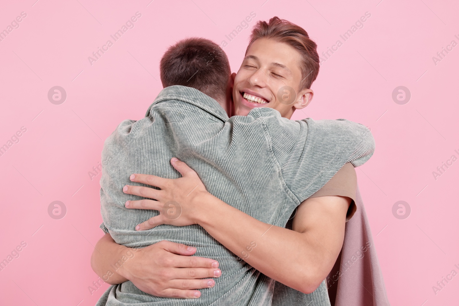 Photo of Two happy friends hugging on pink background
