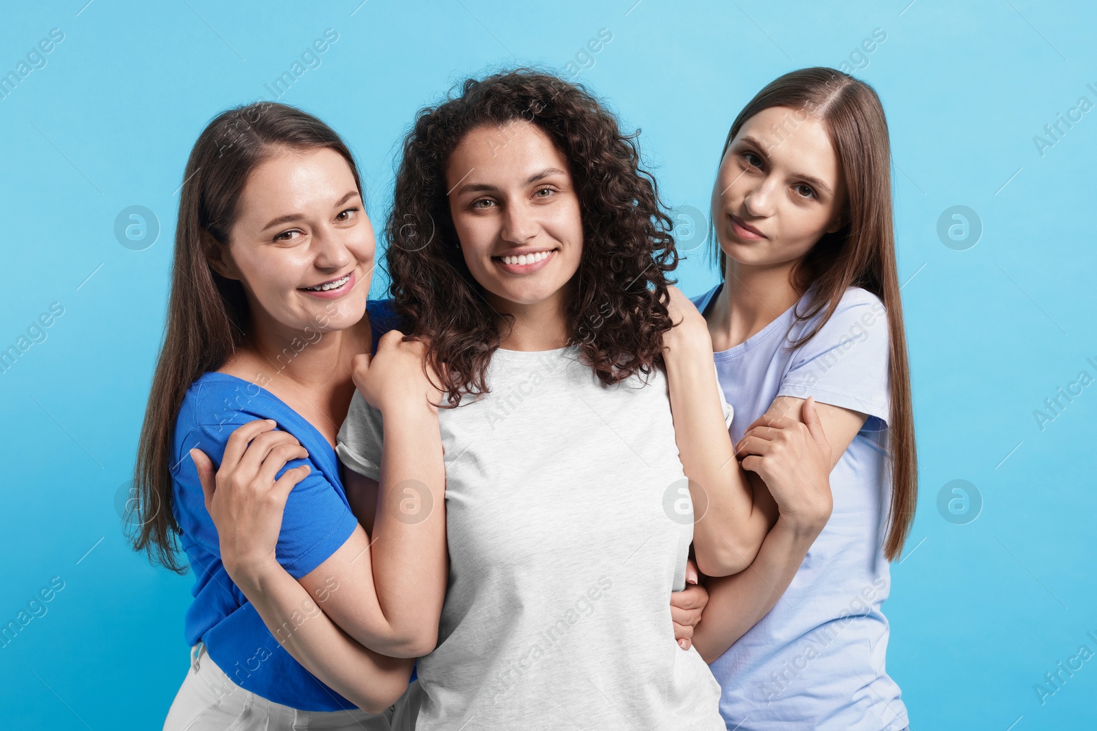 Photo of Three friends hugging on light blue background