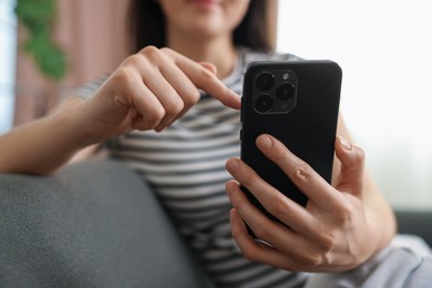 Photo of Woman using modern smartphone on sofa at home, closeup