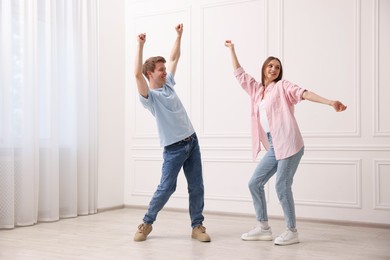 Photo of Happy couple dancing together near white wall at home