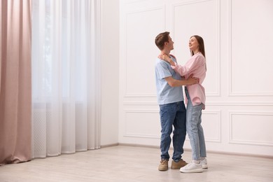 Photo of Happy couple dancing together near white wall at home. Space for text
